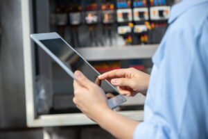 Technician recording switchboard maintenance details on a tablet in front of an open electrical distribution board
